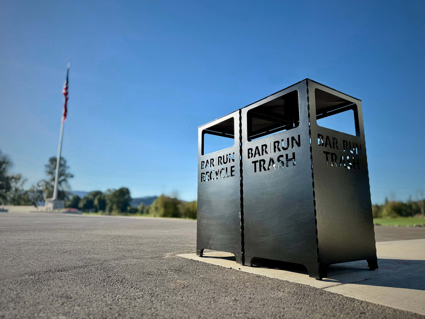 Metal trash and recycling bin on a road with a clear blue sky