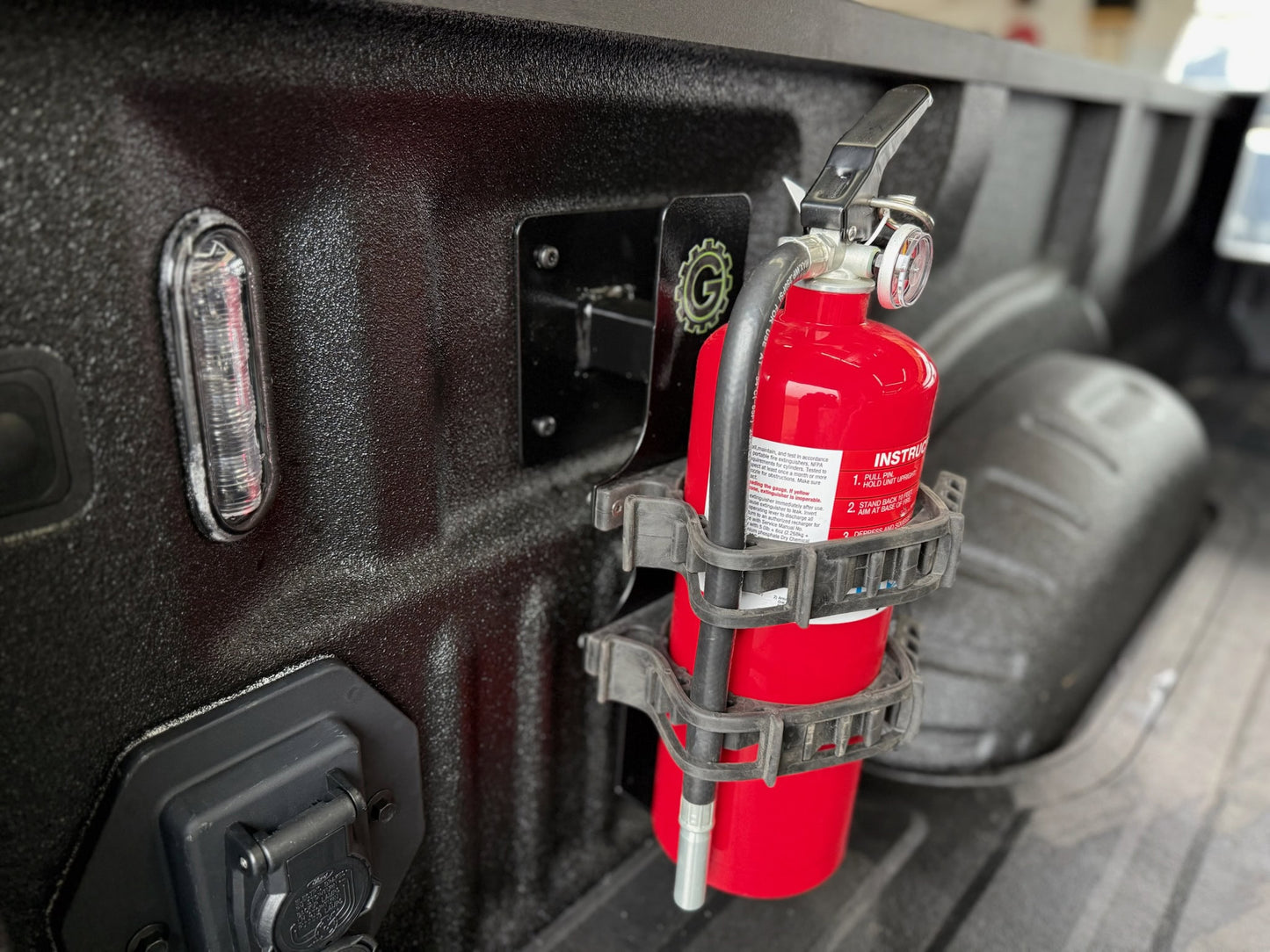Red fire extinguisher mounted on a vehicle's bed with a holder.