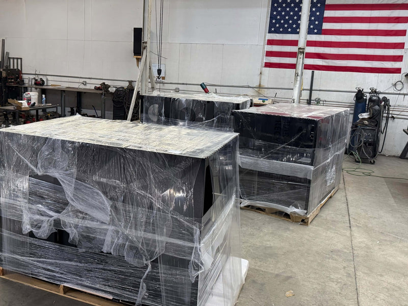 Trash and recycling bins ready to be shipped out in a ware house with an American flag on the wall.