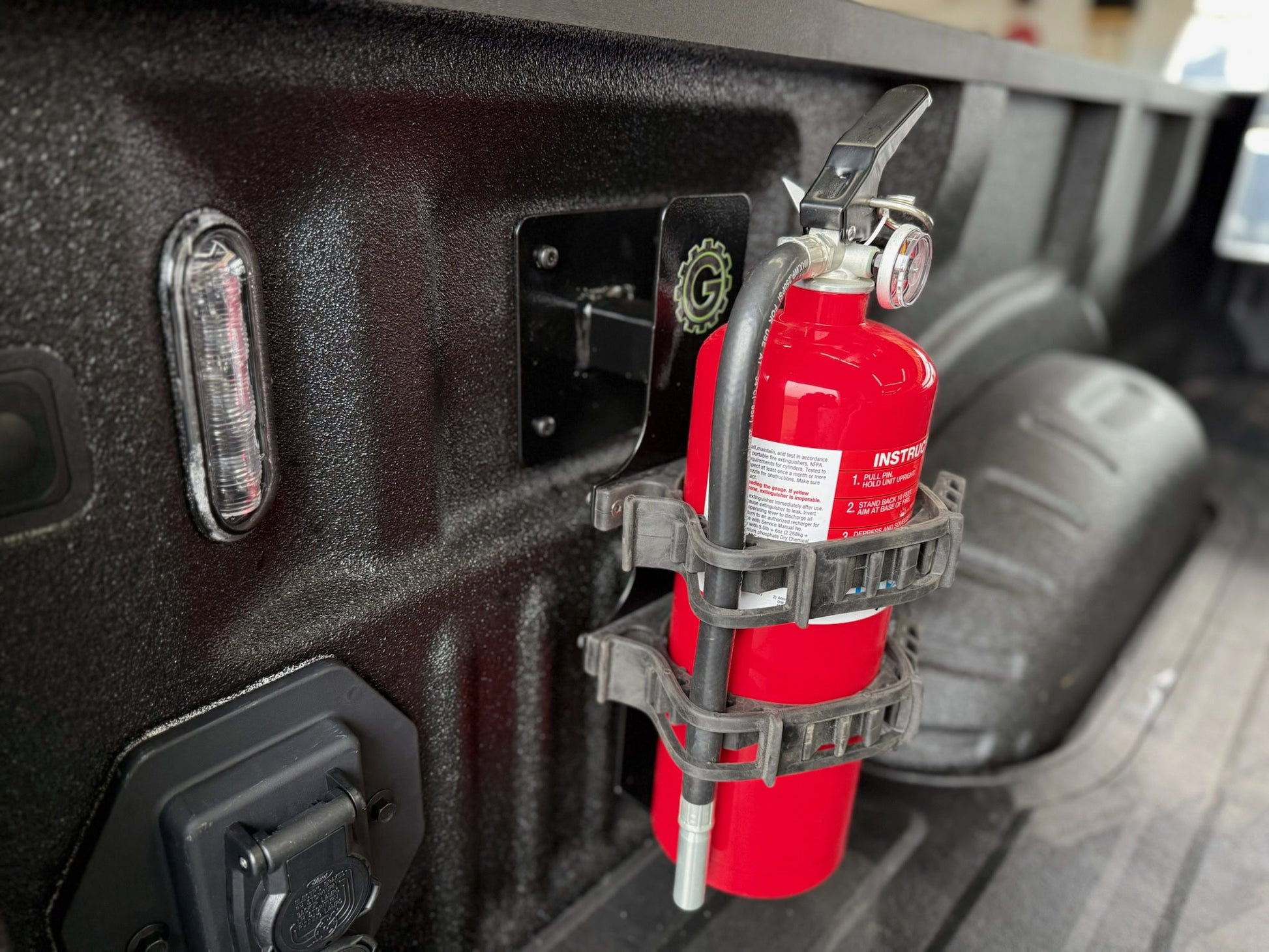 Red fire extinguisher mounted on a vehicle's bed with a holder.